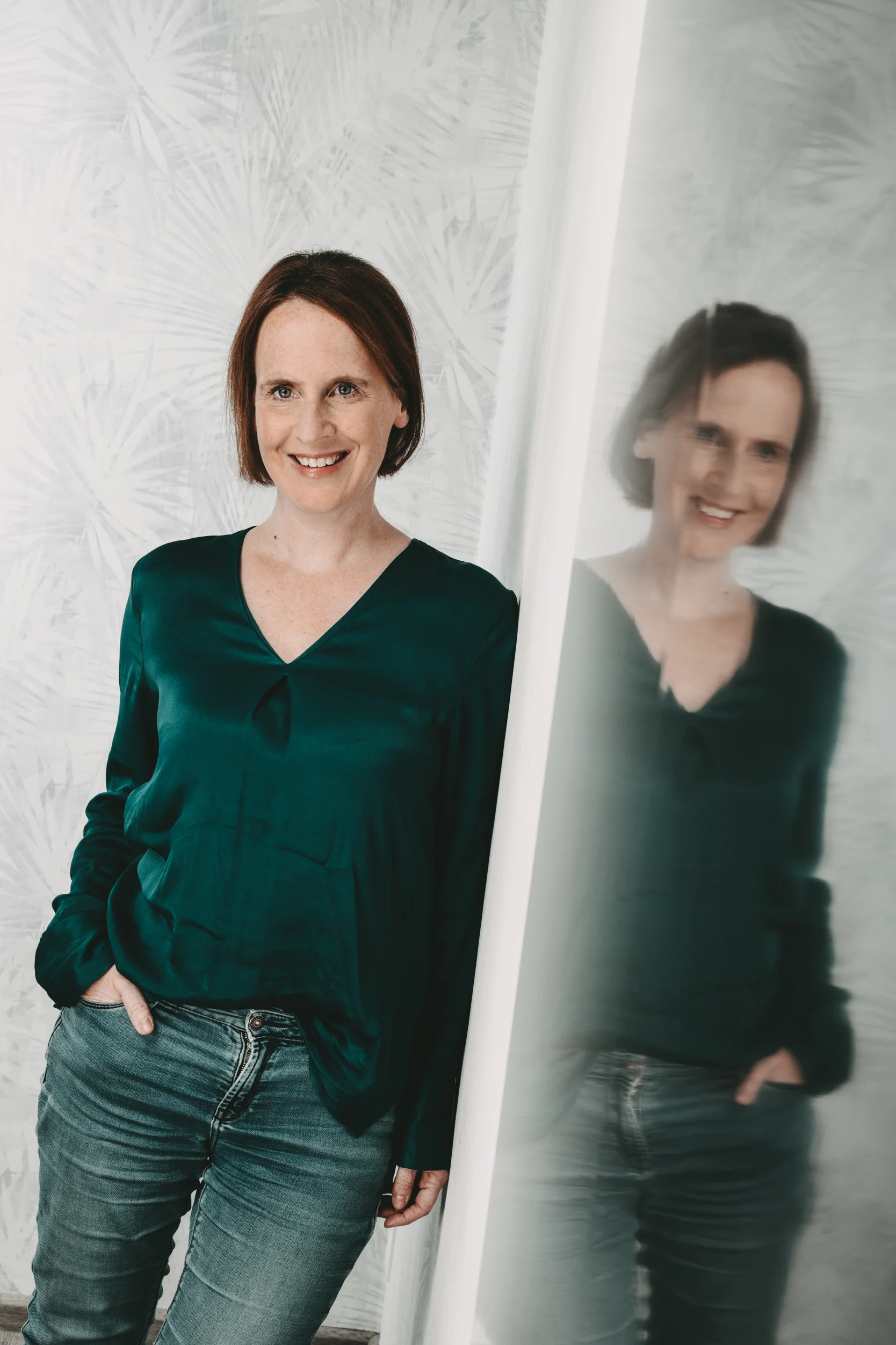 Autorin Nathalie Termer lehnt an einem Spiegel und ist links in echt und rechts im Spiegel zu sehen. 